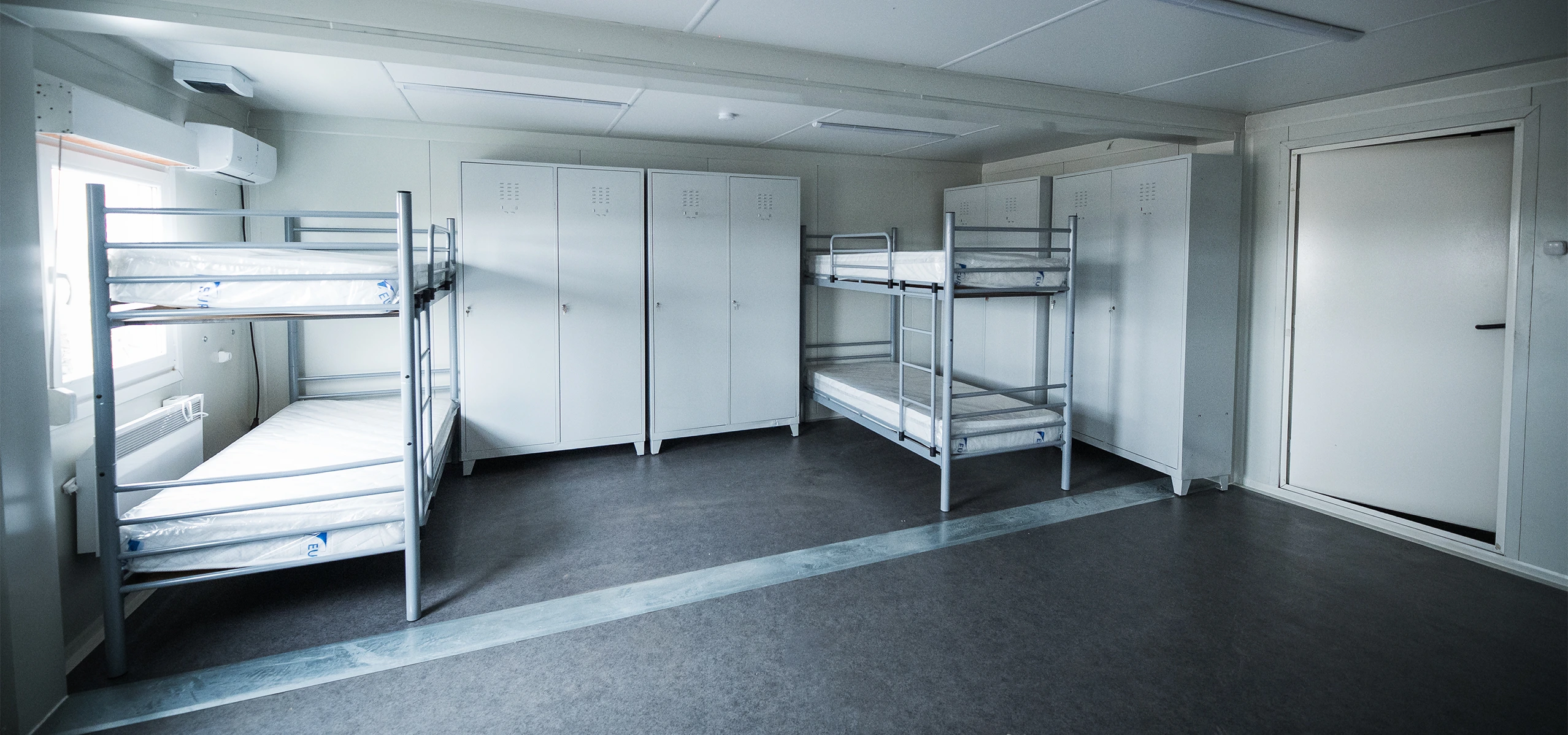 Interior de container modular pentru cazare, echipat cu paturi supraetajate, dulapuri metalice ?i aer condi?ionat.