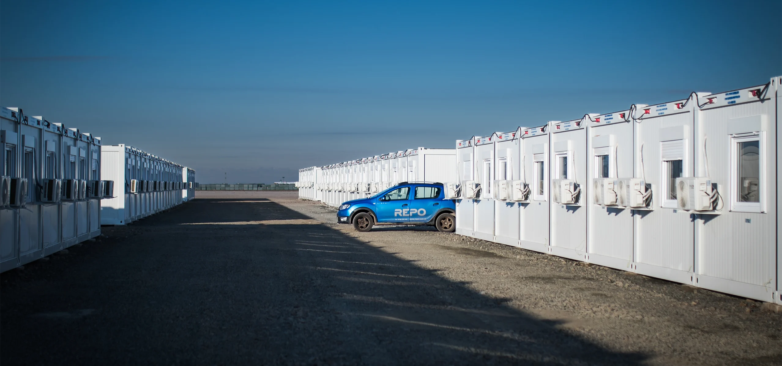Ansamblu de containere modulare albe, echipate cu ferestre ?i aer condi?ionat, instalate într-o baz? temporar?.