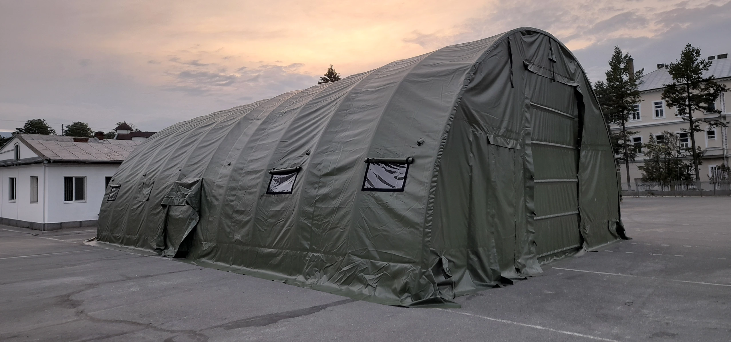 Cort militar tip hangar, cu structur? arcuit? ?i prelat? verde, instalat în exterior.