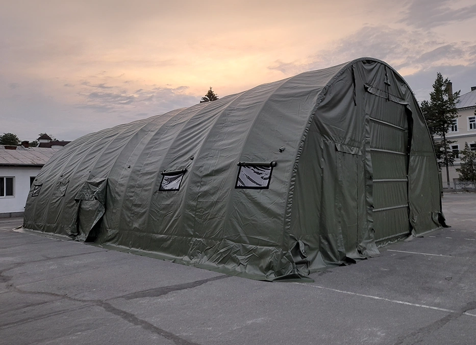 Cort militar tip hangar, cu structur? arcuit? ?i prelat? verde, instalat în exterior pentru utilizare temporar?.